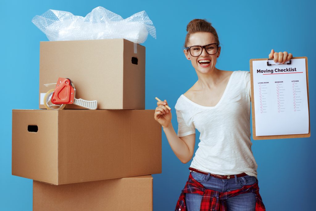 happy woman near cardboard box showing moving checklist on blue
